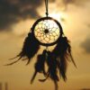 Silhouette of a dreamcatcher hanging against a serene sunset sky.