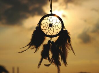Silhouette of a dreamcatcher hanging against a serene sunset sky.