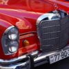 Close-up view of a vibrant red vintage car's front showcasing chrome details and headlight.