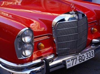 Close-up view of a vibrant red vintage car's front showcasing chrome details and headlight.