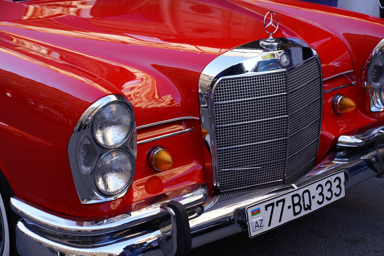 Close-up view of a vibrant red vintage car's front showcasing chrome details and headlight.