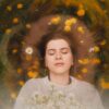 Relaxed woman with closed eyes, surrounded by daisies and dandelions, embracing nature's beauty.