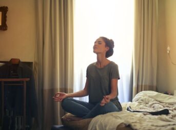 Adult woman practicing meditation on her bed surrounded by a calm bedroom atmosphere.