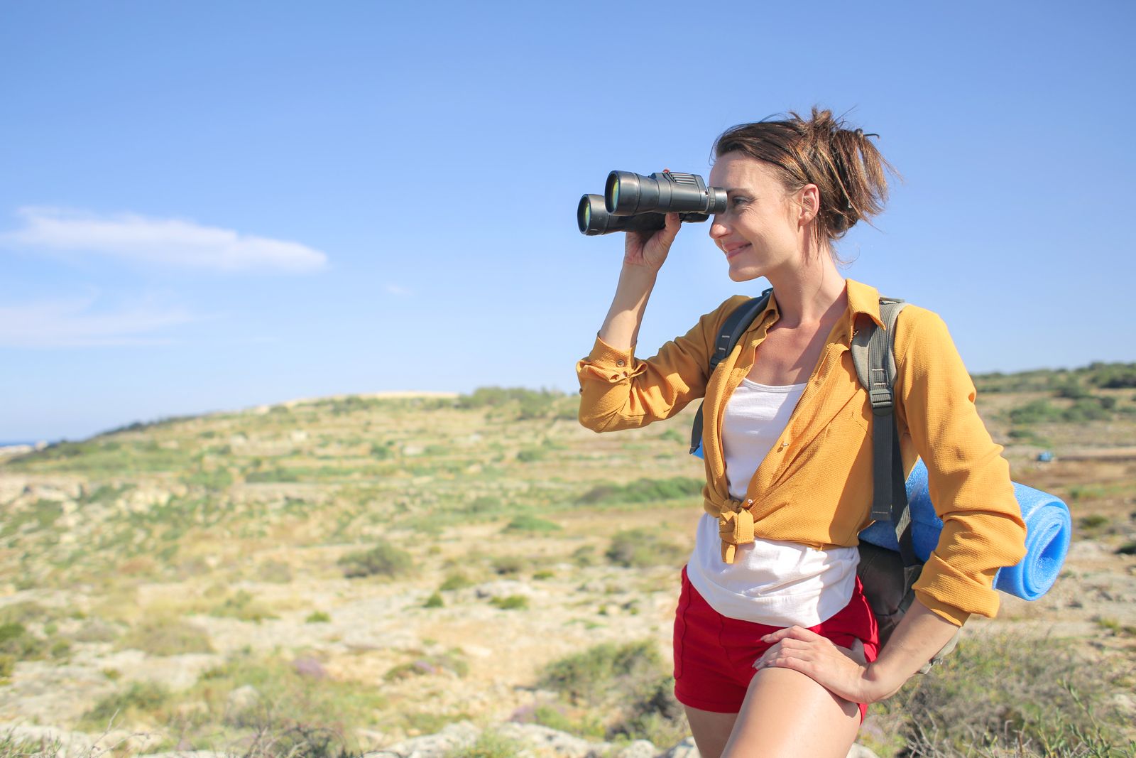 Young woman enjoying a sunny day hike, using binoculars to explore nature and capture the scenic view.