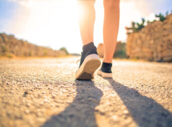 A woman walks down a sunlit path in summer, highlighting leisure and travel outdoors.