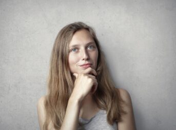 A thoughtful woman contemplates life in a simple portrait with a gray background.