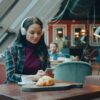 Woman using phone and listening to music while sitting in a modern cafe.