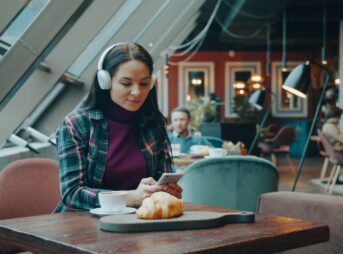 Woman using phone and listening to music while sitting in a modern cafe.