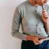 Crop unrecognizable female worker in casual clothes standing with clipboard and notebook and touching chin with pen against white wall