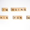 Wooden Scrabble tiles spell 'I'm doing this for me' on a white surface.