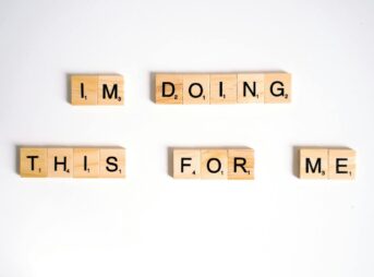 Wooden Scrabble tiles spell 'I'm doing this for me' on a white surface.