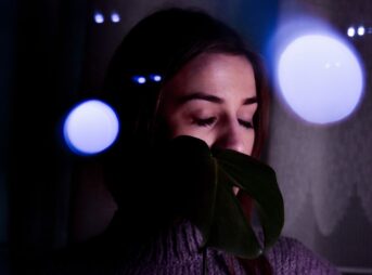 Concentrated young female in gloves and sweater with long eyelashes on closed eyes at dusk