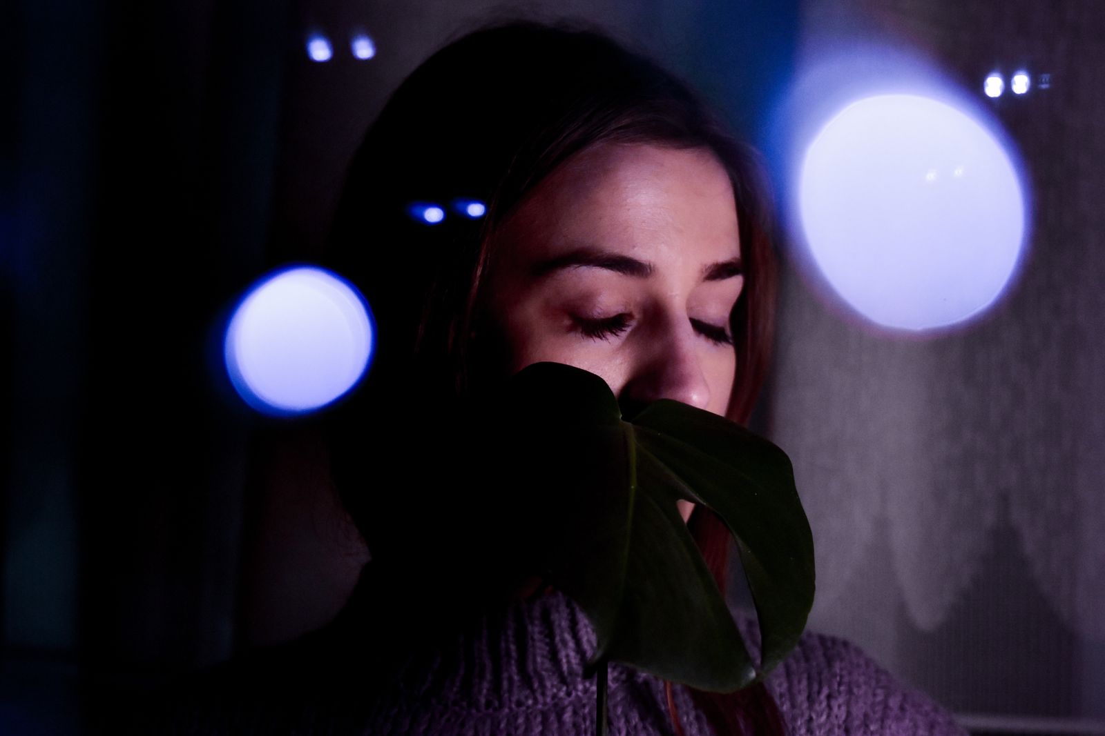 Concentrated young female in gloves and sweater with long eyelashes on closed eyes at dusk