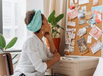African American woman reflecting on a vision board by a window with plants.