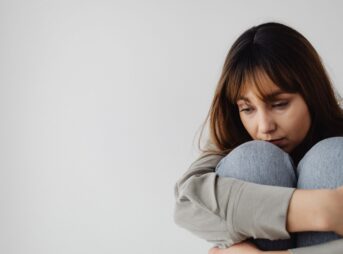 Caucasian woman sitting pensively indoors, capturing a moment of reflection and emotion.