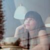 Thoughtful woman gazing outside a café window with reflections and warm lighting.