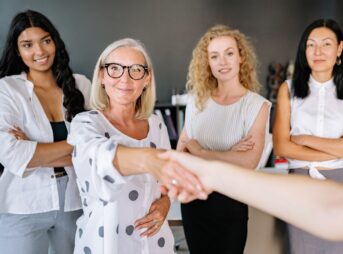 Diverse group of women in an office setting shaking hands and smiling, symbolizing partnership.