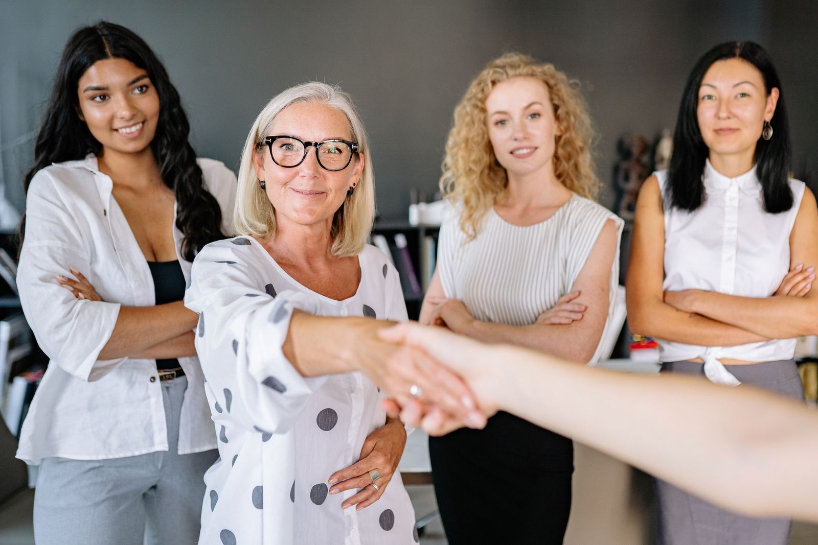 Diverse group of women in an office setting shaking hands and smiling, symbolizing partnership.