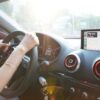 Hands on steering wheel using GPS navigation inside car during road trip.