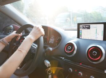 Hands on steering wheel using GPS navigation inside car during road trip.