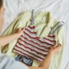 Woman arranging a stylish blazer and knitted top outfit on a bed.
