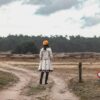 a woman standing on a dirt road in a field