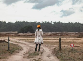 a woman standing on a dirt road in a field