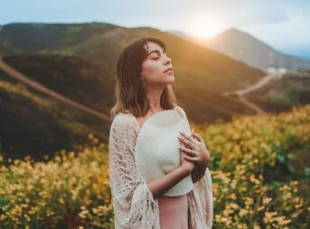 woman holding white hat while standing on yellow flower field