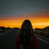 woman in red and black plaid shirt standing on road during sunset