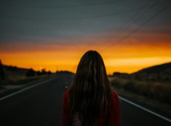 woman in red and black plaid shirt standing on road during sunset