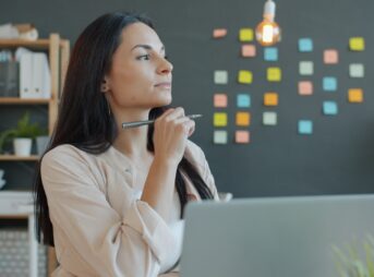 A woman thinking with a pen at her desk