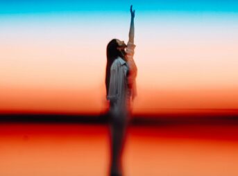 Woman reaching up against colorful sunset sky