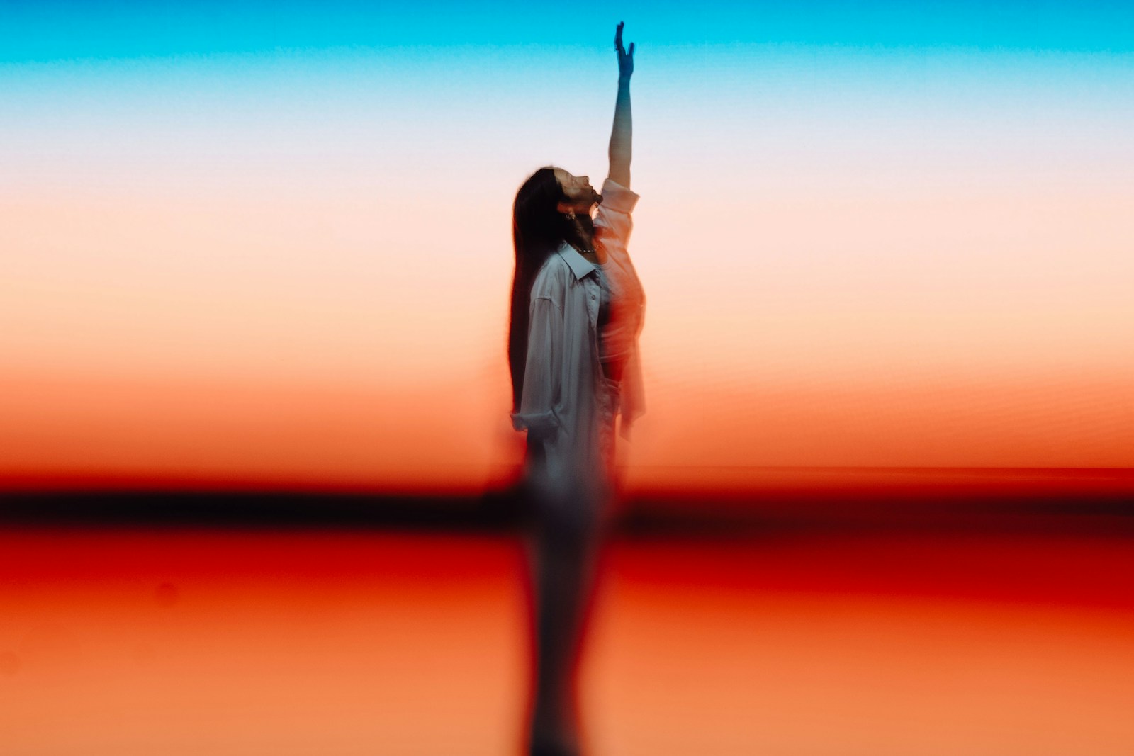 Woman reaching up against colorful sunset sky