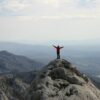 man in red long sleeve shirt standing on gray rock formation during daytime