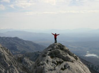 man in red long sleeve shirt standing on gray rock formation during daytime