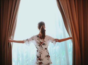 woman in black and white floral dress standing near window