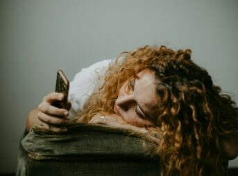 woman in gray sweater holding smartphone