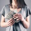 woman in gray shirt holding fan of us dollar bills