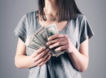 woman in gray shirt holding fan of us dollar bills