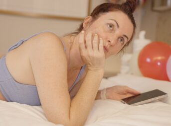 Woman lying on bed with phone and balloons