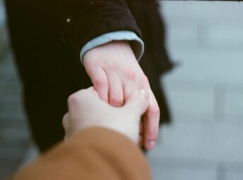 person in black long sleeve shirt holding babys hand