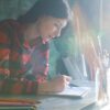 Woman in plaid shirt drawing at desk with pencils