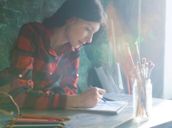 Woman in plaid shirt drawing at desk with pencils