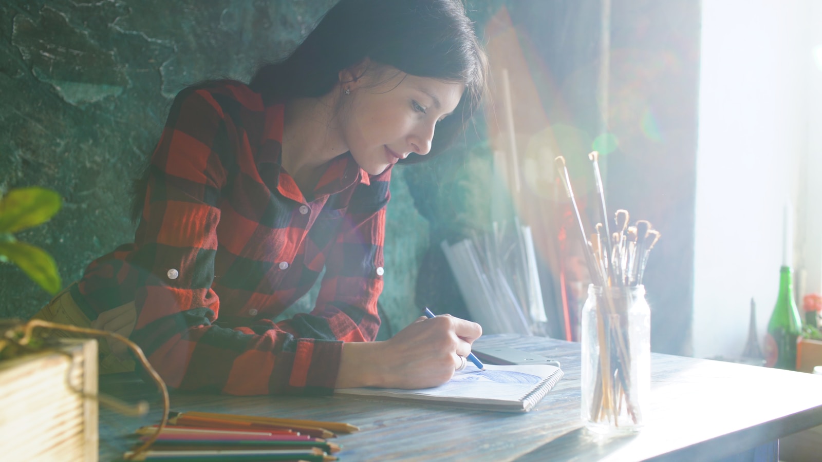Woman in plaid shirt drawing at desk with pencils